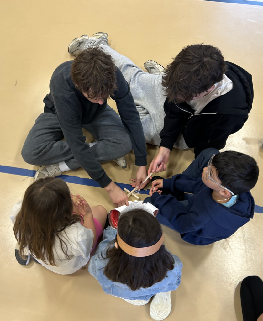 Two middle school boys in a group with elementary students working on a STEM activity