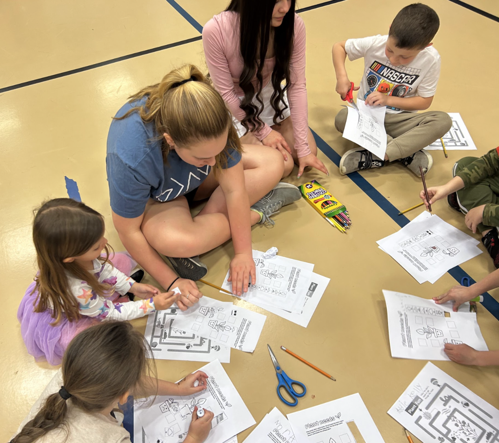 Two middle school girls in a group with elementary students working on a STEM activity