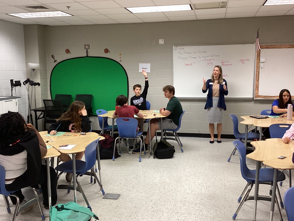 Woman asking questions, students looking at her, one boy raising his hand