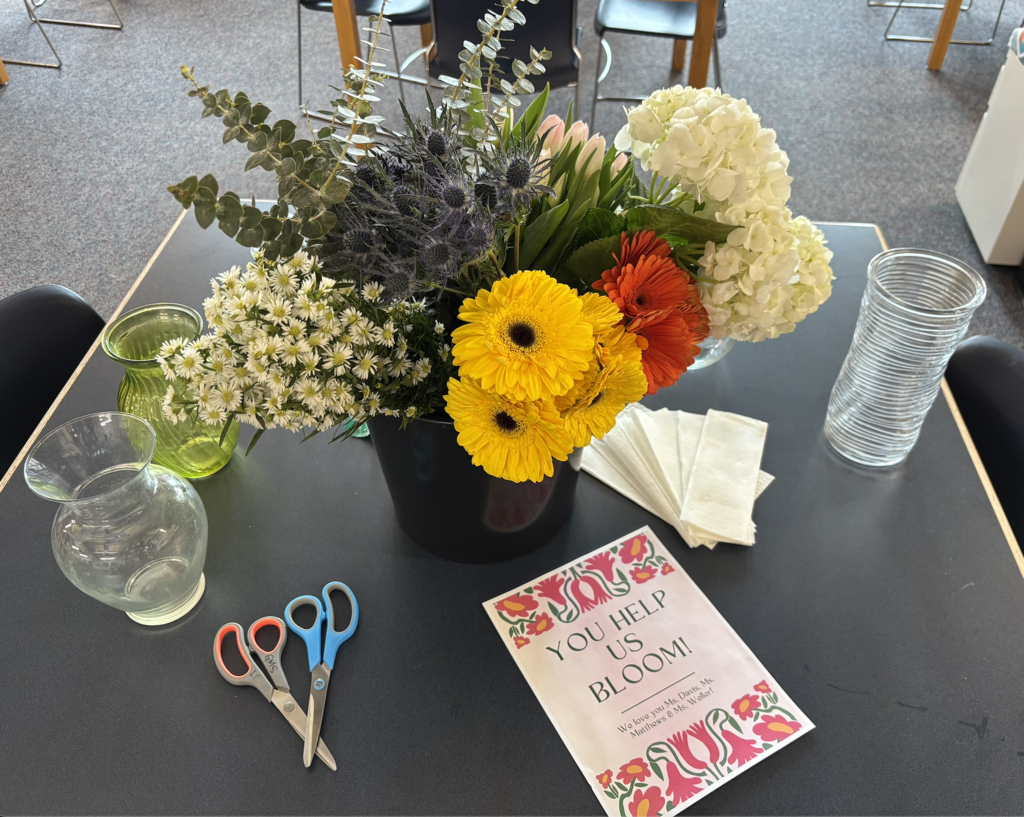 Bouquet set up with flowers, vases, scissors, and a 'You Help Us Bloom!' flyer