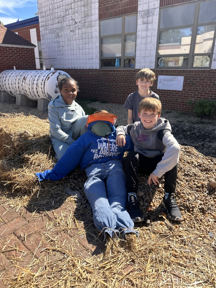 three kids sitting with the scarecrow they made