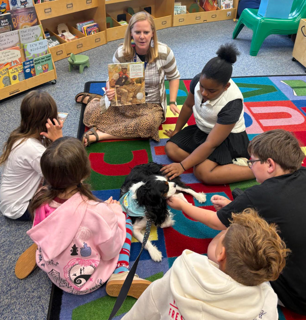 Librarian holding story for students to see while they pet the Reading Therapy Dog
