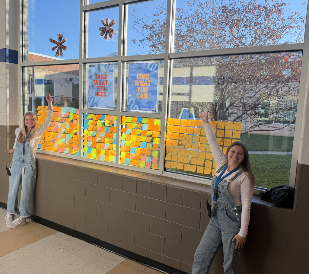 Ms. Harlow and Ms. Powell with the Take What You Need, Give What You Can wall