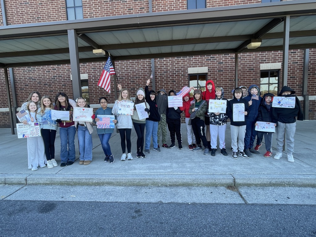 A group of students holding flags and signs celebrating veterans.