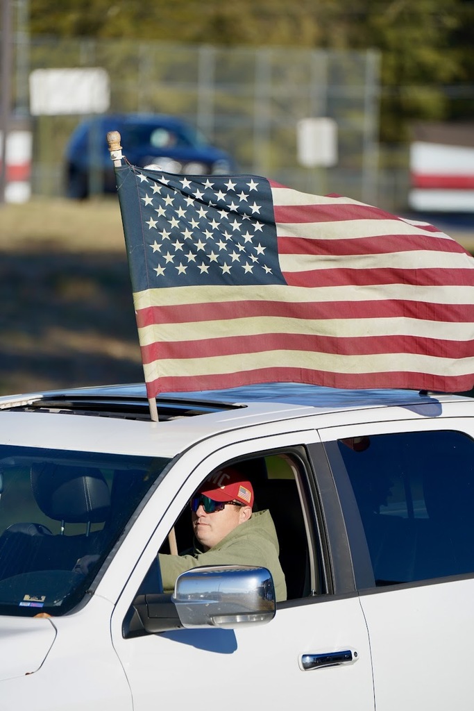 A man in a white truck flying an american flag.