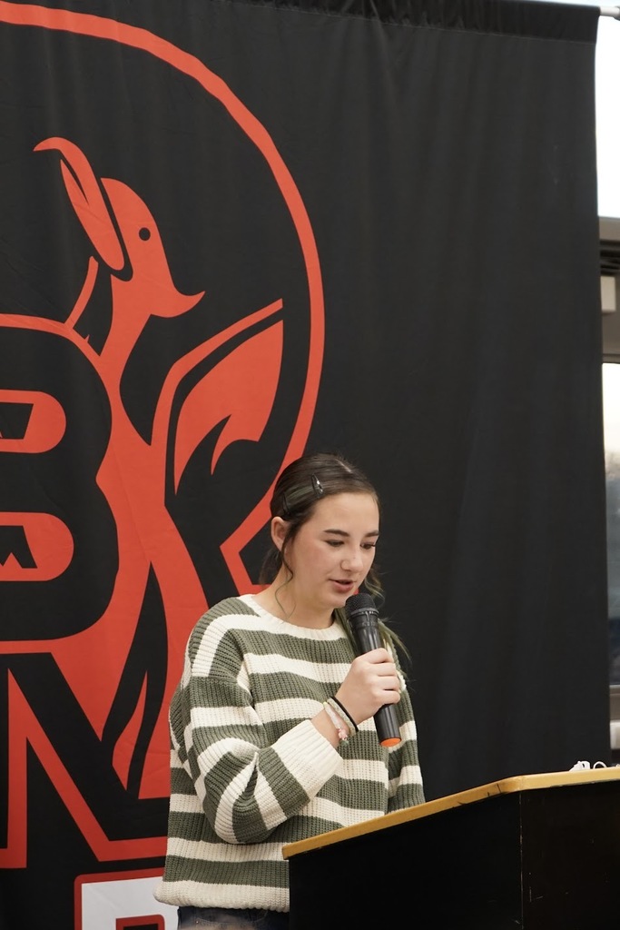 A student wearing a striped shirt reading her writing piece.