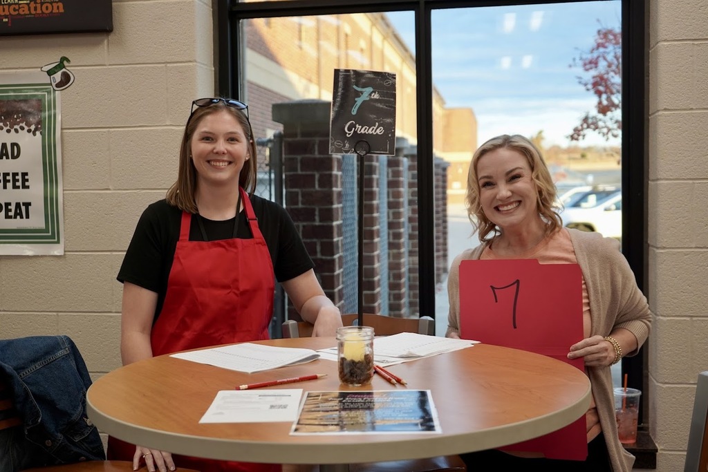 2 teachers wearing red aprons manning a table for literacy night.