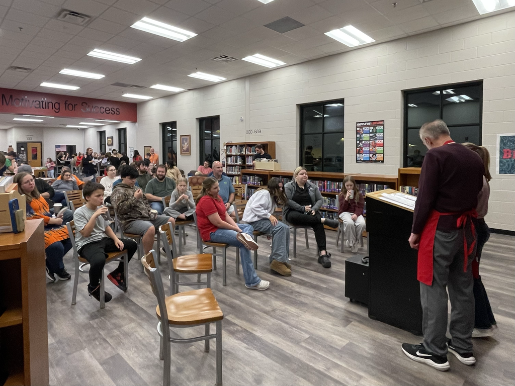 A group of parents listening to students read their literary works.