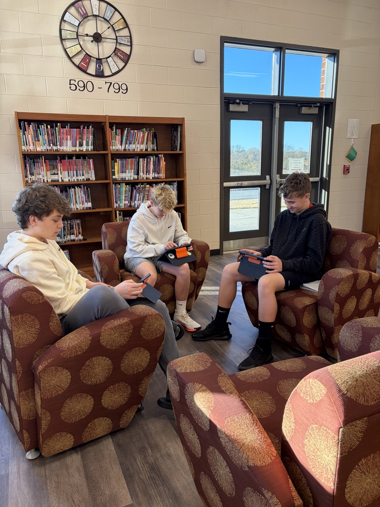 Three boys writing poetry while sitting in chairs.