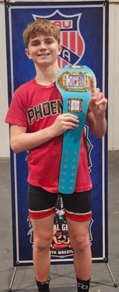 A middle school boy holding a wrestling award belt.