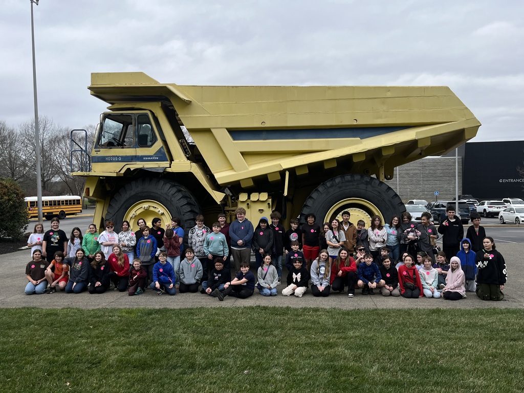 students posing in front of an enormous yellow dump truck outside the museum
