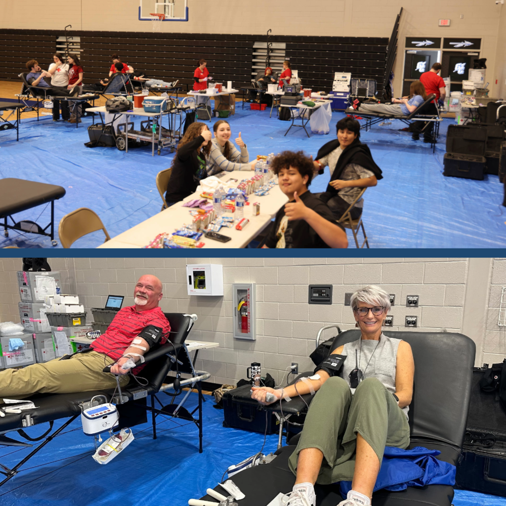 Students and community members participate in a blood drive inside a school gym. In the foreground, several students sit at a table giving thumbs up. In the background, donors sit on medical cots while people assist them. Two people are donating blood.