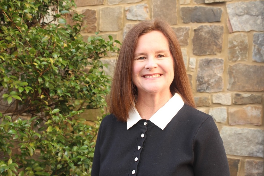 Becky Hulsey standing in front of a green bush and stone wall.
