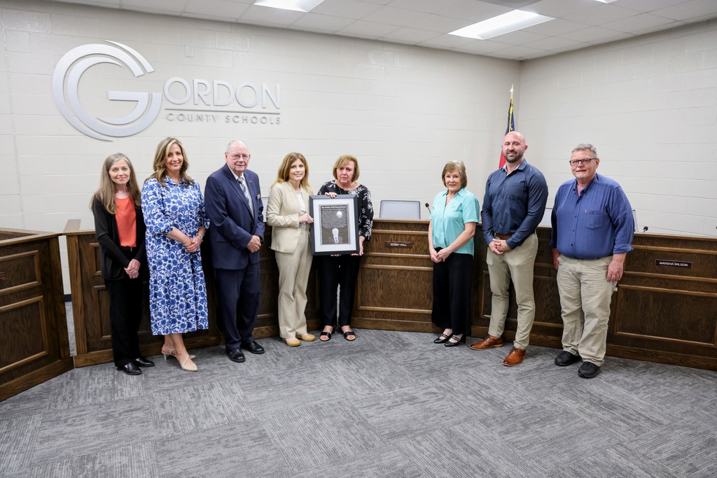 Board of Education members along with the family of Bobby Hall accepting the framed mock-up of his plaque honoring the renaming of the Board Room.