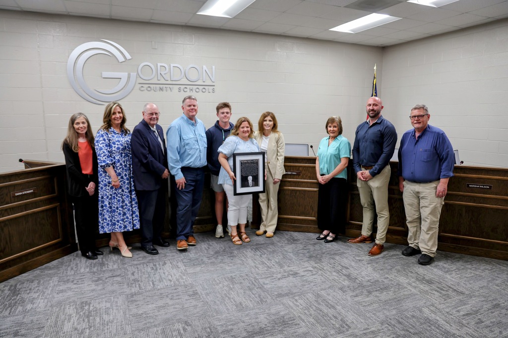 Board of Education members along with the family of Bobby Hall accepting the framed mock-up of his plaque honoring the renaming of the Board Room.