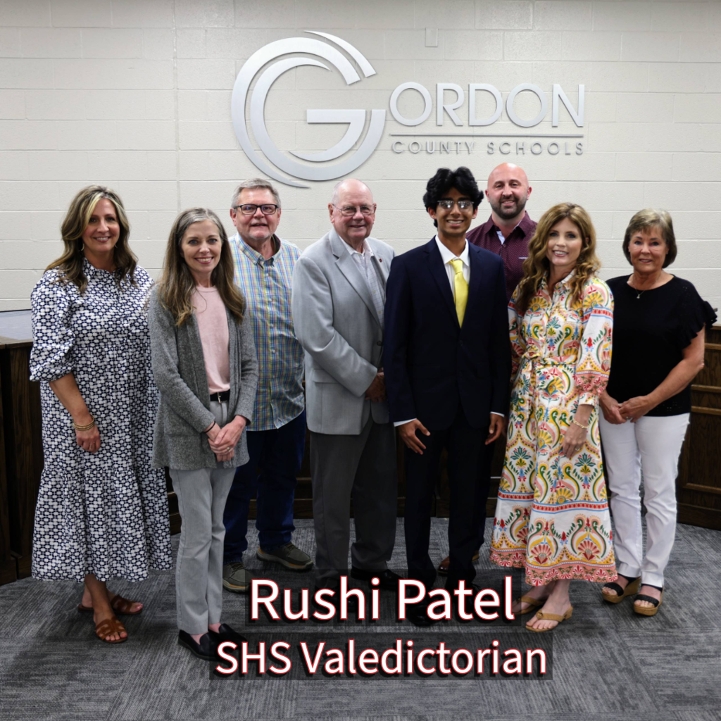 SHS Valedictorian Rushi Patel with GCS Board of Education members in front of a Gordon County Schools logo