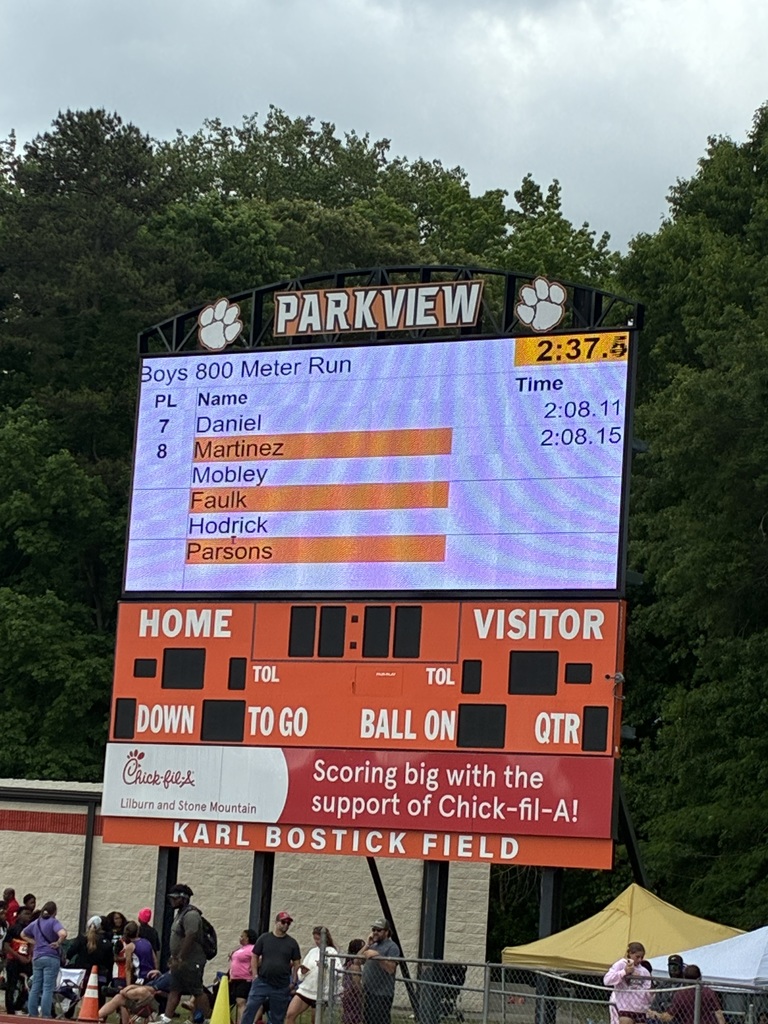 Large stadium scoreboard displaying “Boys 800 Meter Run” results with runner names and finishing times, labeled “Parkview,” above a crowd standing near the field.