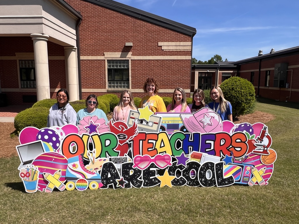 7 female third grade teachers standing behind a yard sign reading "our teachers are cool"