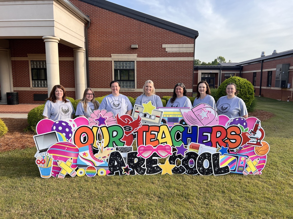 7 female kindergarten teachers standing behind a yard sign reading "our teachers are cool" 