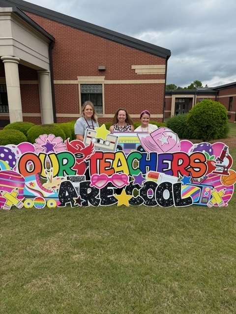 Support Teachers standing behind a yard sign reading "our teaches are cool"