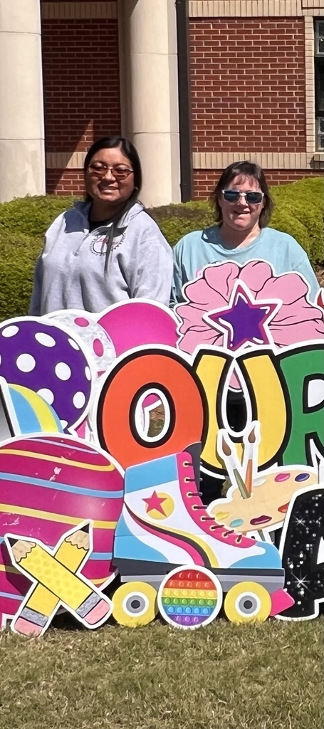 Two support teachers standing behind a yard sign. The picuture is cropped and sign is unreadable. 