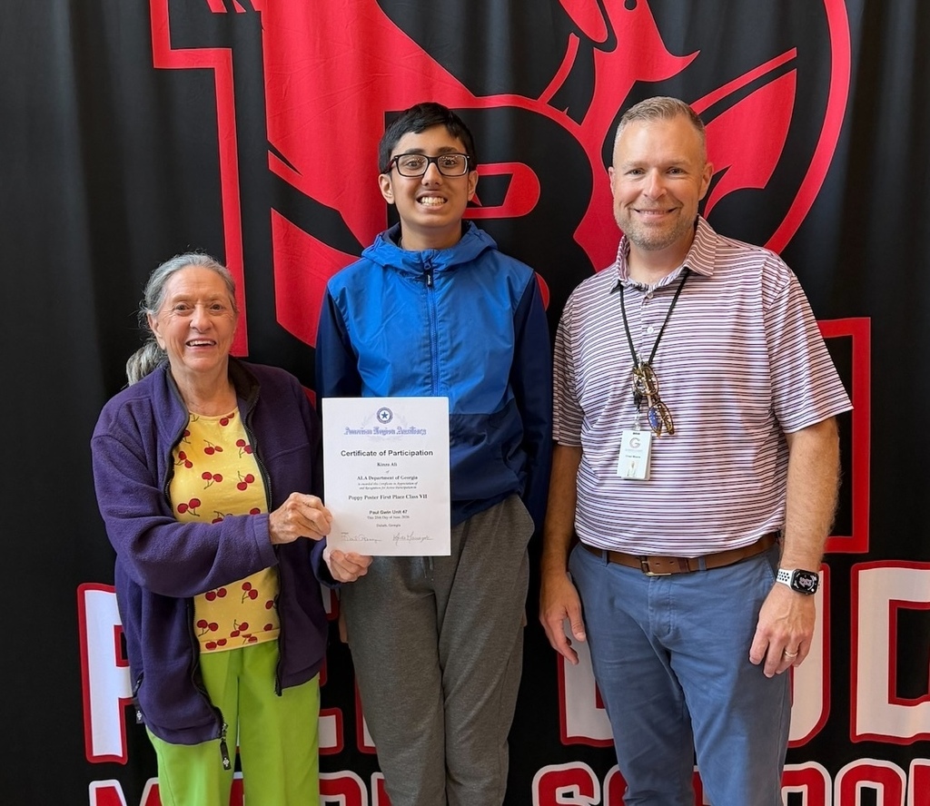A lady wearing a yellow shirt and purple jacket is presenting a student wearing a blue jacket a certificate. A man with a striped polo shirt stands to the right.