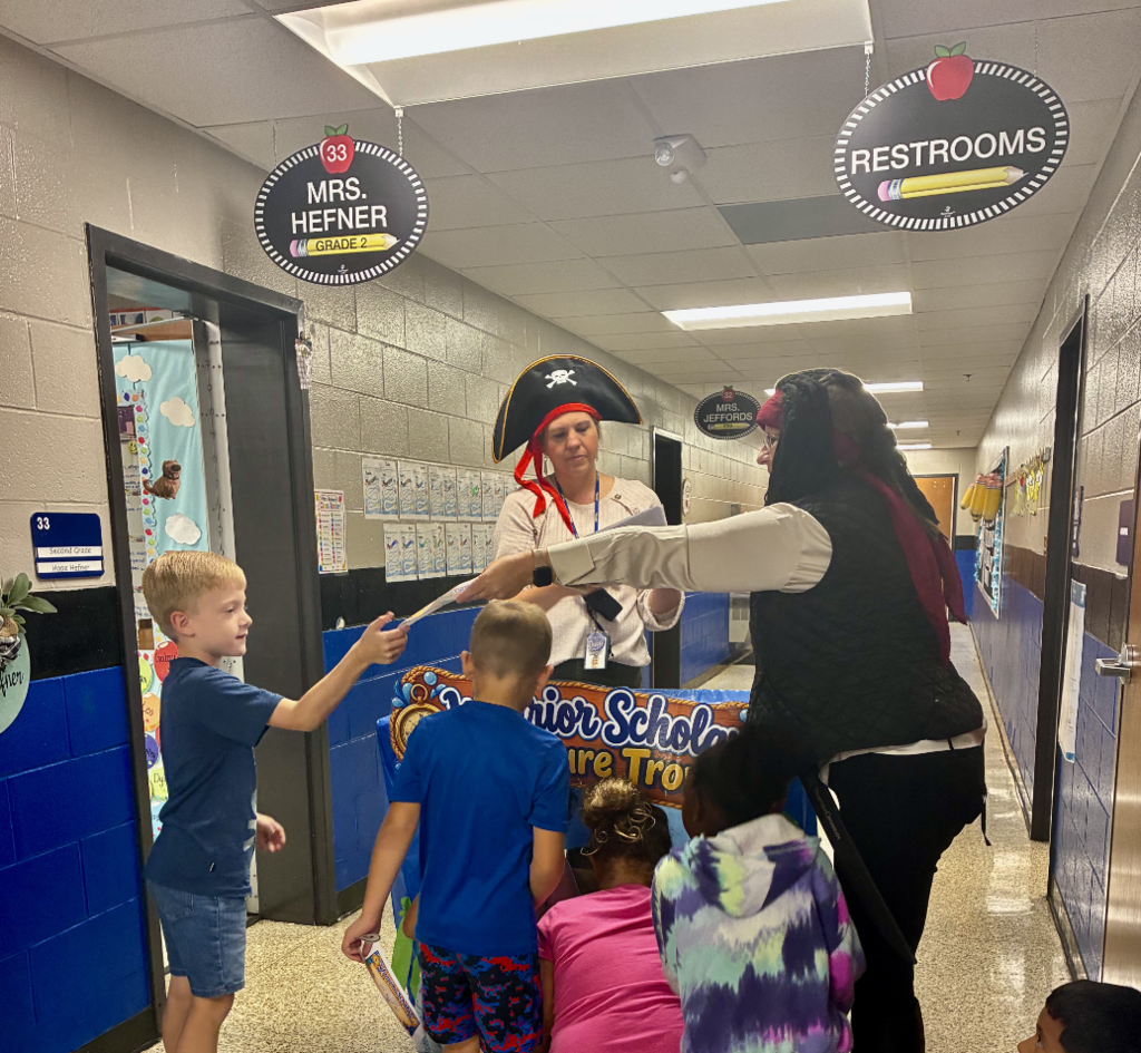 Tolbert Elementary staff members dressed as pirates present certificates to students gathered around the Warrior Scholar Treasure Trove treat cart in the school hallway.