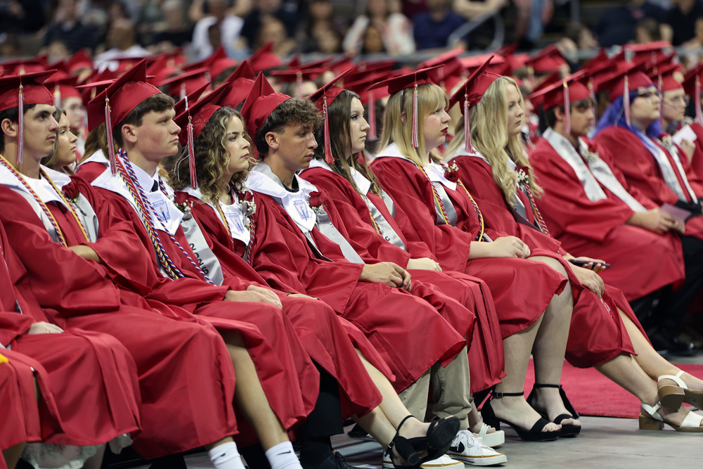 students seated wearing red caps and gowns