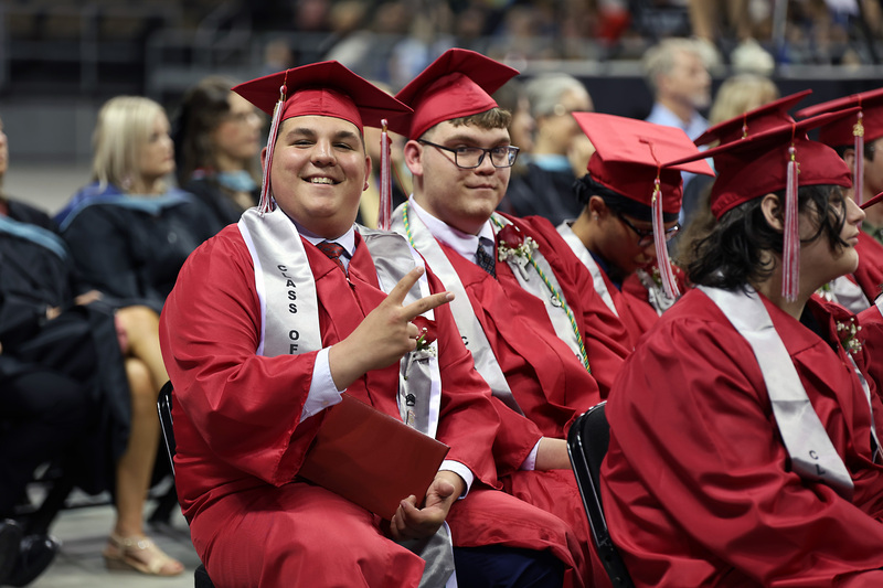 student in camp and gown waving to camera