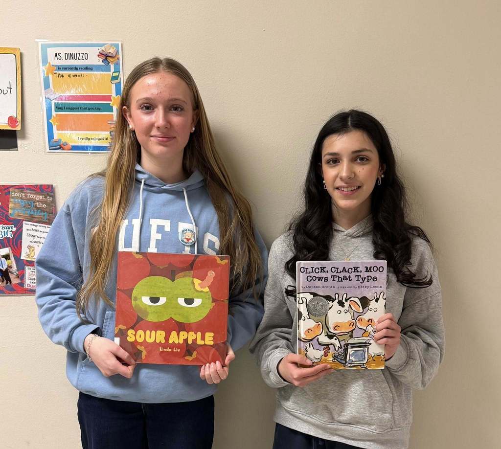 Two students are holding up the books they read to students at Wells Road School
