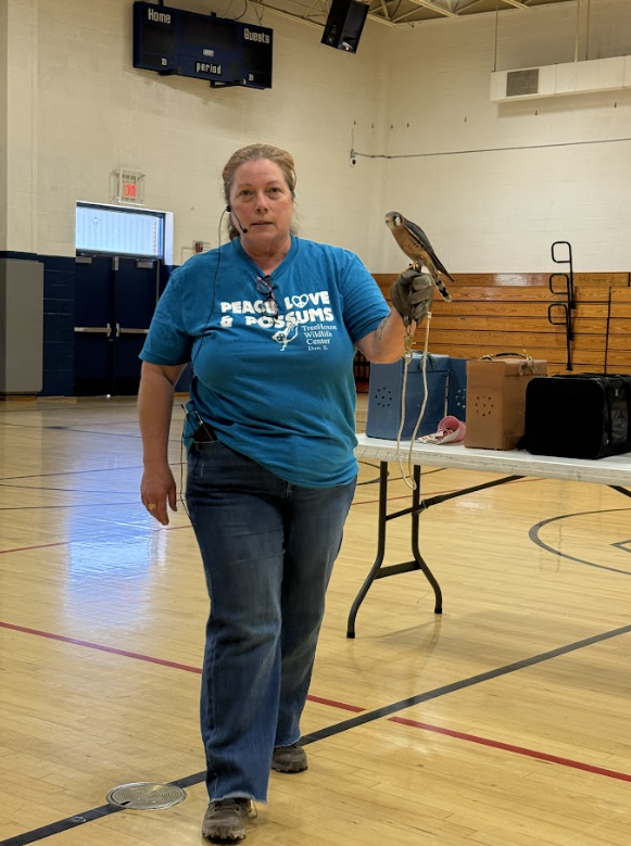 Volunteer from rescue facility with a bird of prey in front of students at an assembly