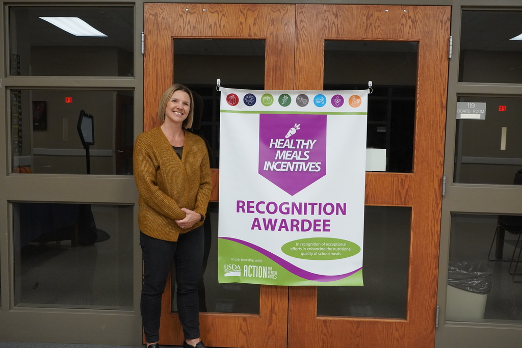 Woman in brown cardigan next to award banner