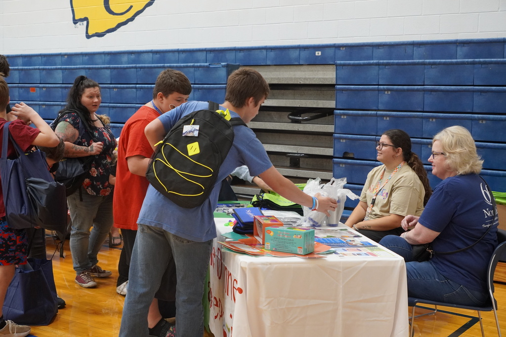 table with school bleachers, boys with backpack and two women