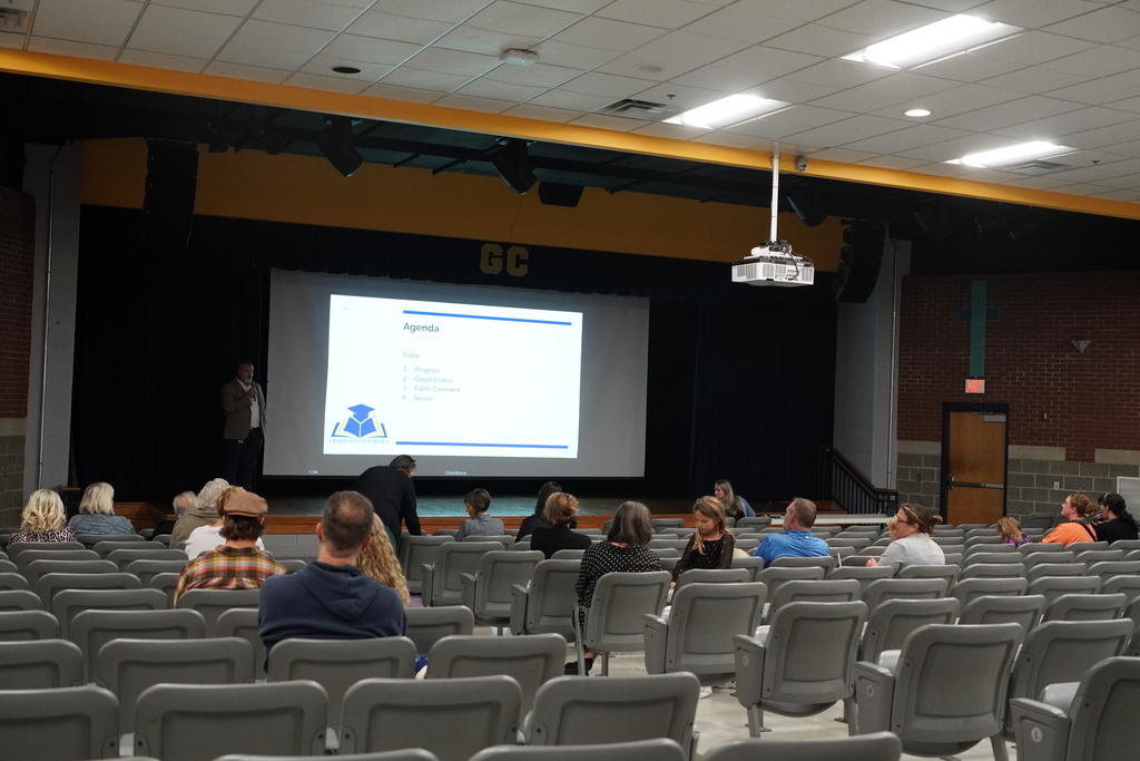auditorium of people, projector screen, man presenting