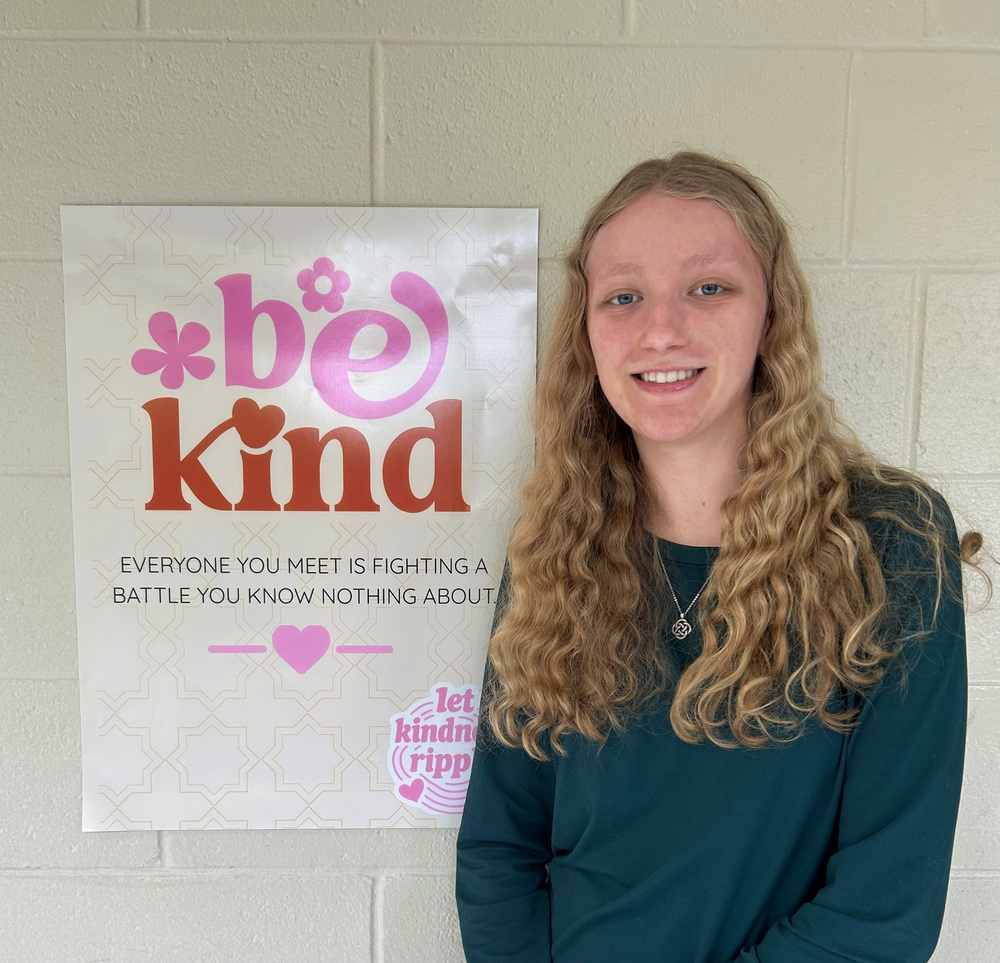 The author, Addison ManWarren standing next to one of her posters that says: Be kind. Everyone you meet is fighting a battle you know nothing about. Let Kindness Ripple. 