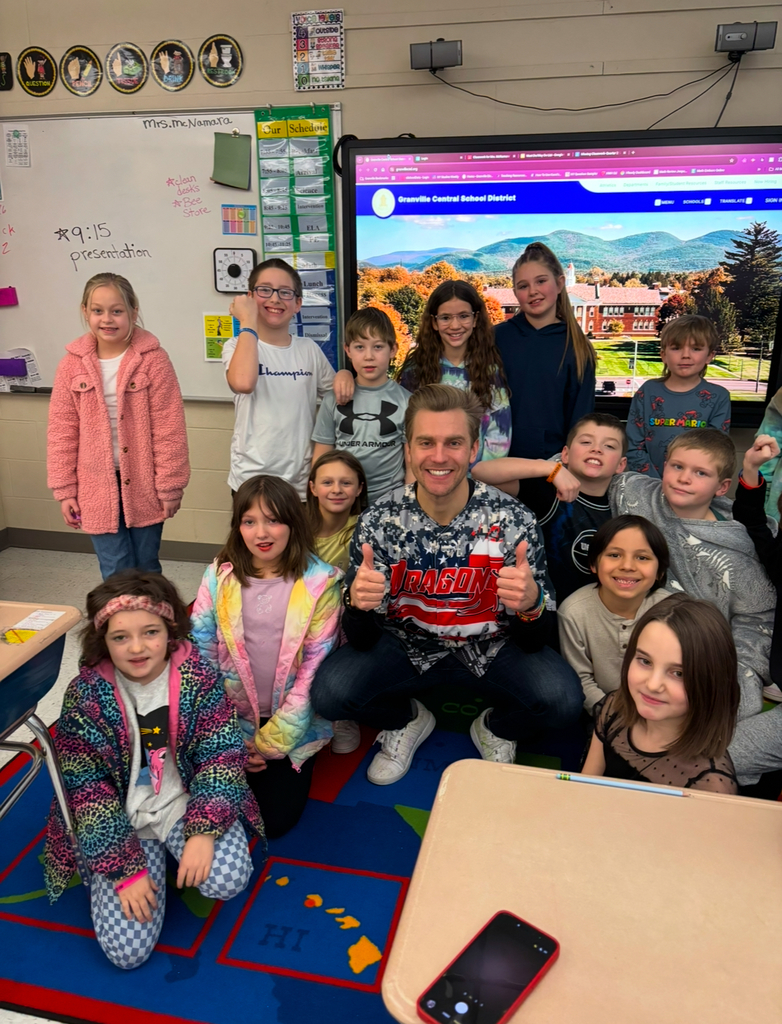 Billy Floyd is centered with a group of elementary students in a classroom. 