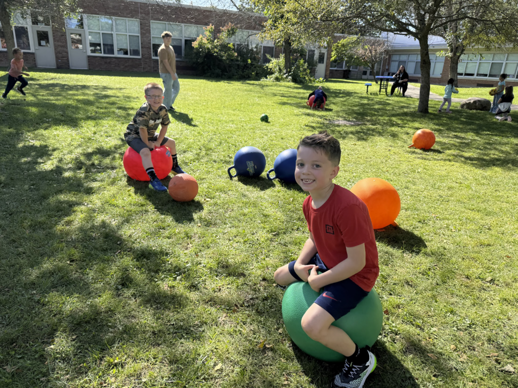 Two boys in the afterschool program at MJT bounce on outdoor bouncy chairs in the outdoor courtyard at MJT