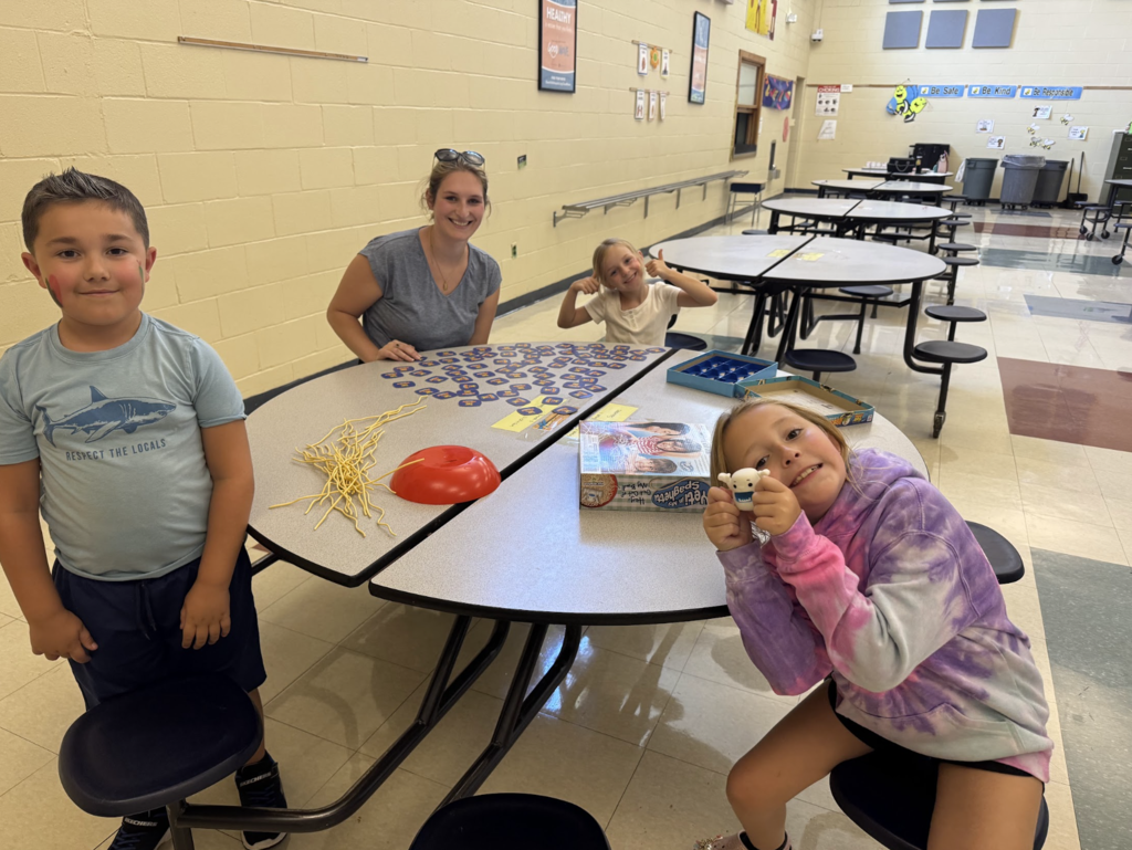 Two students and a teaching assistant play an educational game in the cafeteria at the MJT afterschool program