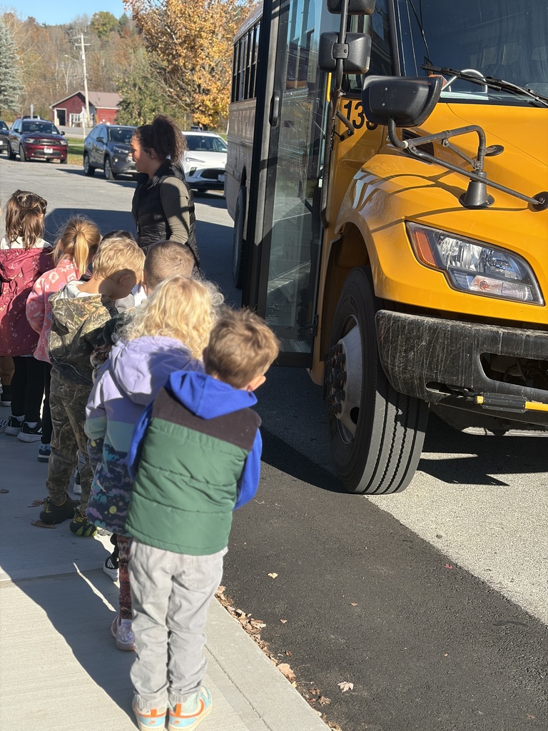 A group of students at MJT stand near a school bus and listen to a lesson about school safety