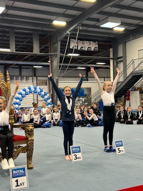 Ella Mead at a Gymnastics Tournament - Arms raised high with medals around her neck. 