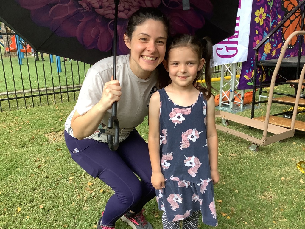 A young girl poses with her mom under an umbrella.