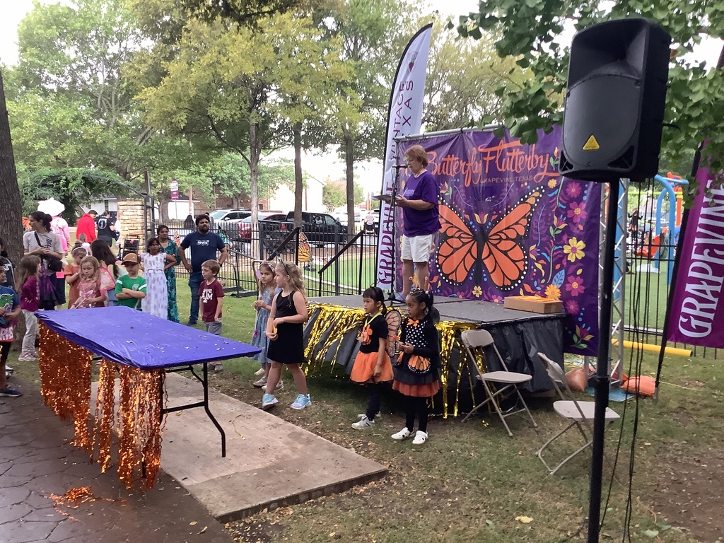 A group of kids stands in front of a stage decorated with butterfly imagery. 