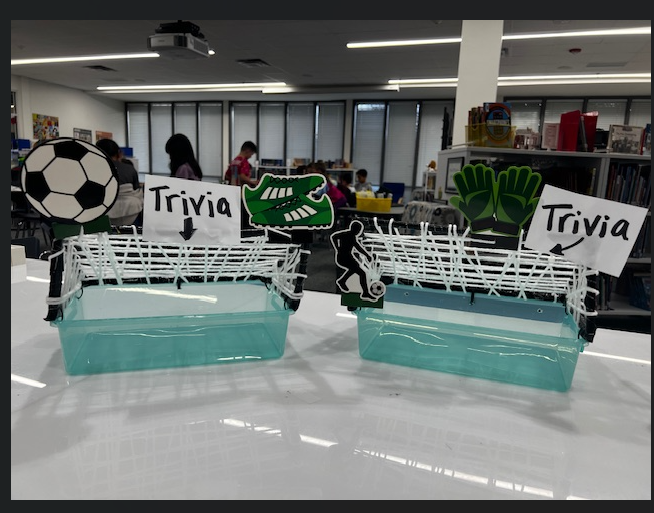 Picture contains two green boxes that have been decorated to look like soccer goals. Both have signs on them saying "Trivia" with an arrow pointing to where the slips should go.The background is the library windows.