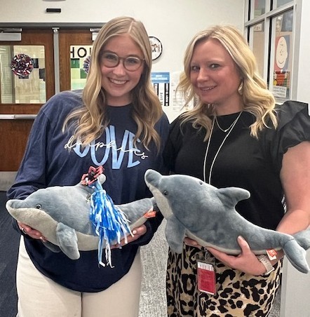 two women holding stuffed dolphins in the library