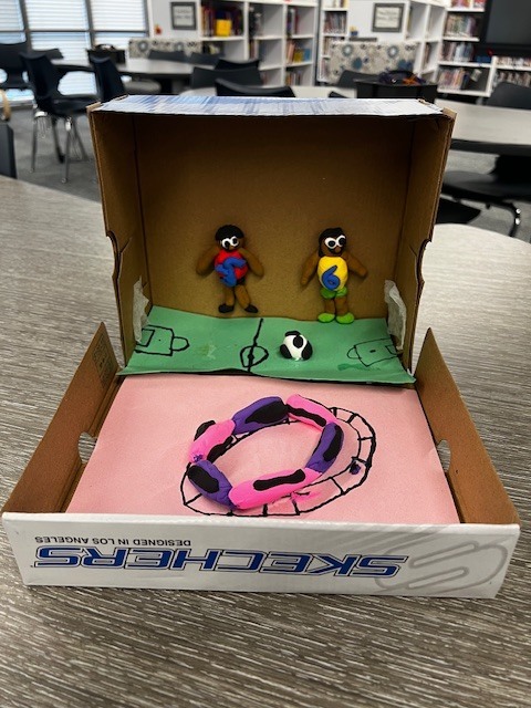 shoebox with a paper soccer field and two clay soccer players