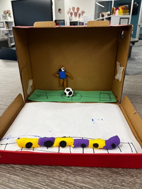 cardboard box with a green paper soccer field, a clay person and a clay soccer ball