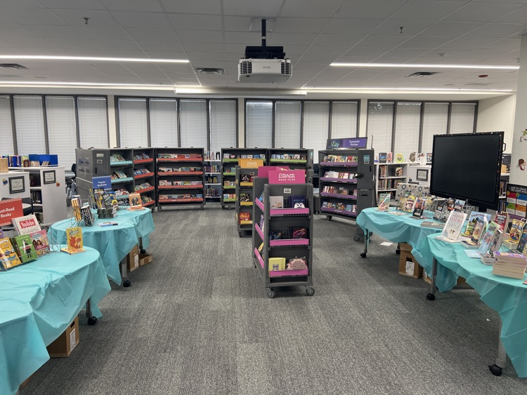 library with large cases of books, four tables with blue tablecloths and books sitting on them
