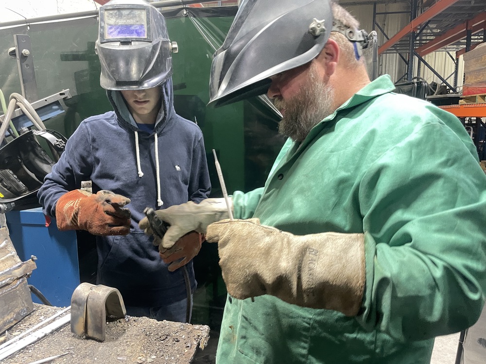 YOUNG MAN AND WELDING INSTRUCTOR LOOK AT A WELD PRACTICE JOB 