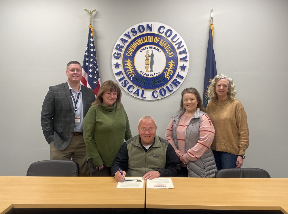 Josh Baldwin, Barbara Allen, GC Judge Executive Kevin Henderson, Shalee Watson and Kim Cannon at a table before a proclamation signing