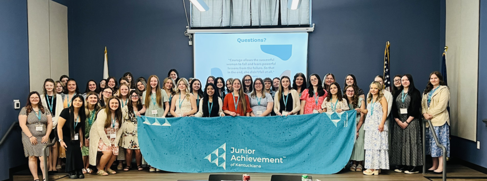 GCHS female students at a girls conference on stage holding a junior achievement banner